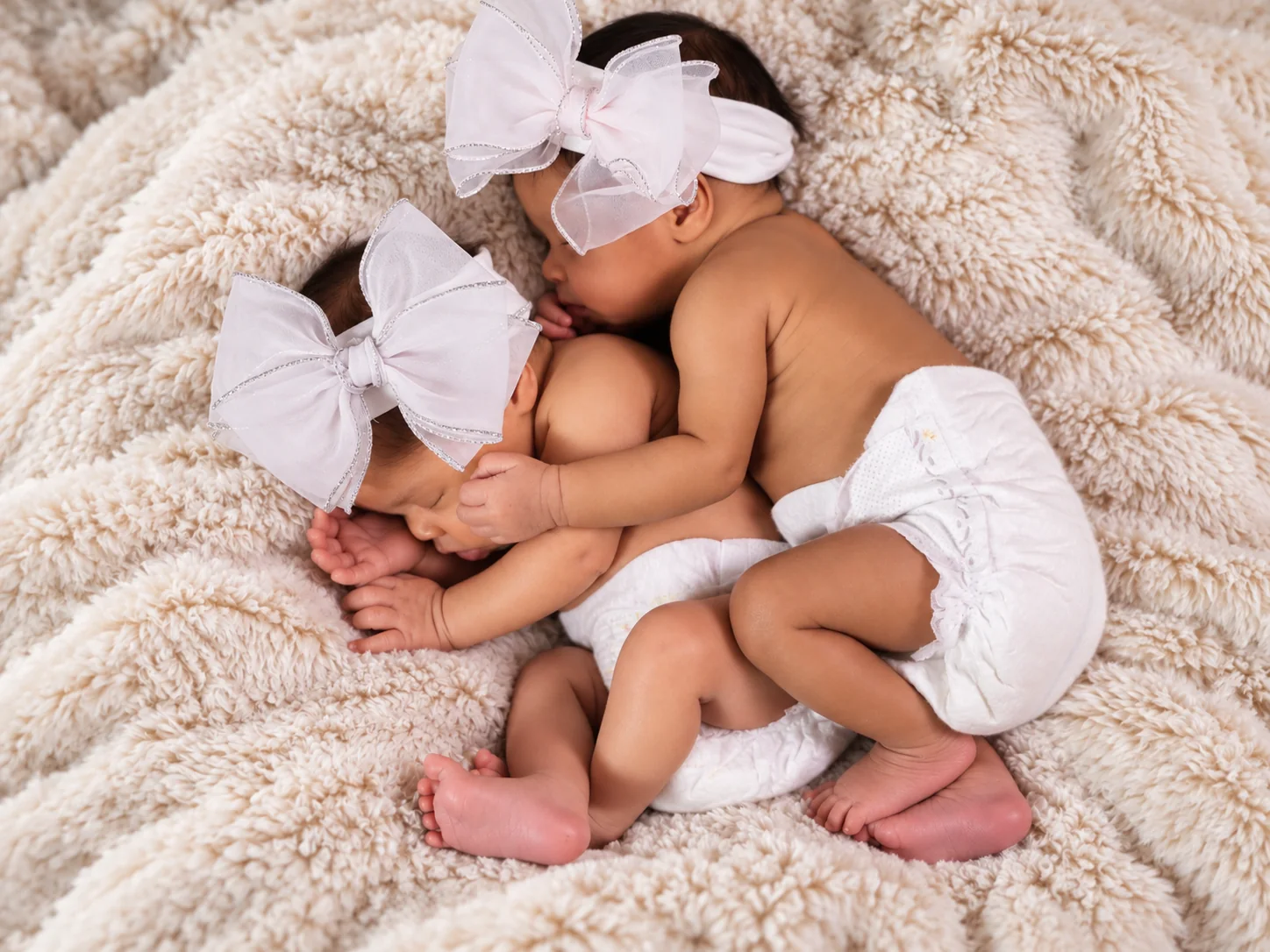Sleeping newborn twins embracing in a soft studio setting